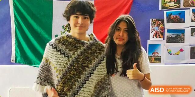 Two smiling students from QSI International School of Zhuhai posing together in a warm, textured shawl.