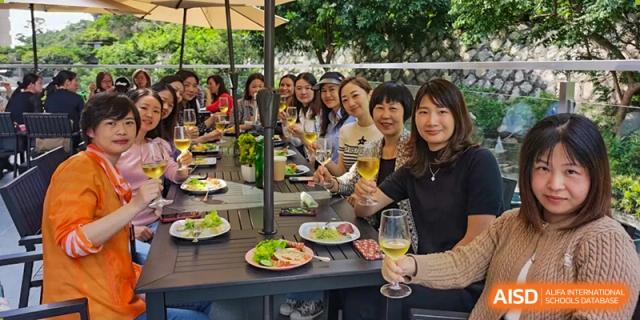 A group of female staff members or parents at QSI International School of Zhuhai having an outdoor lunch or social gathering at a picnic table.