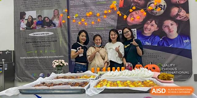 A group of female staff members or parents at QSI International School of Zhuhai posing next to a table filled with catered snacks and a decorative background.