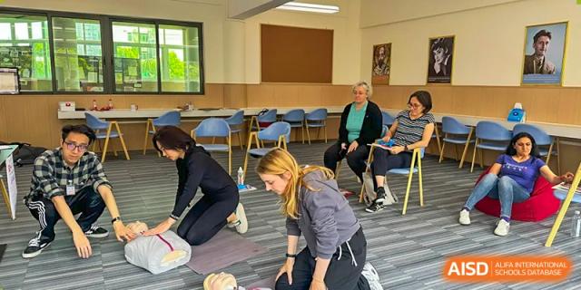 A first aid or CPR training session taking place at QSI International School of Zhuhai, with staff members practicing on the floor.