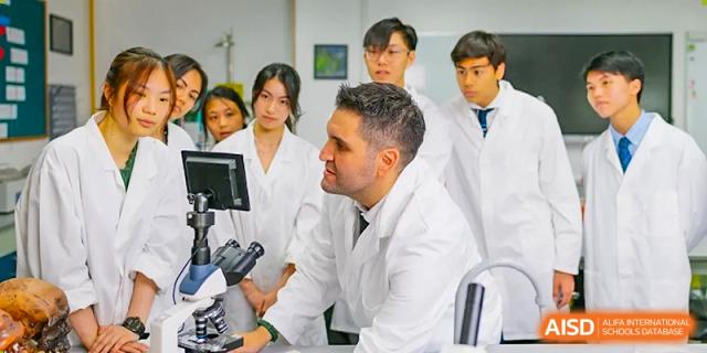 An image showing students in lab coats looking at a microscope with a teacher at Wellington College International Shanghai.