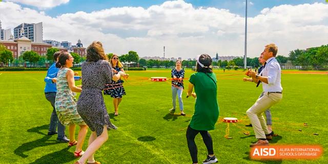 An image showing a group of people playing a game with ropes on a grassy field at Wellington College International Shanghai.