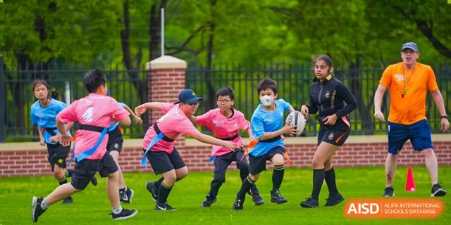 An image showing two boys playing with a rugby ball on a green field at Wellington College International Shanghai.