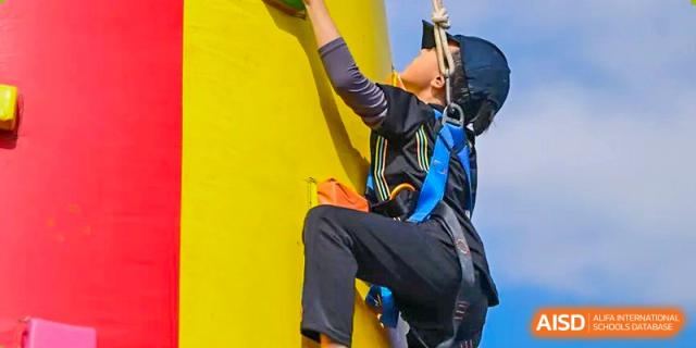 An image showing a person rock climbing on a yellow wall while wearing a safety harness at Wellington College International Shanghai.