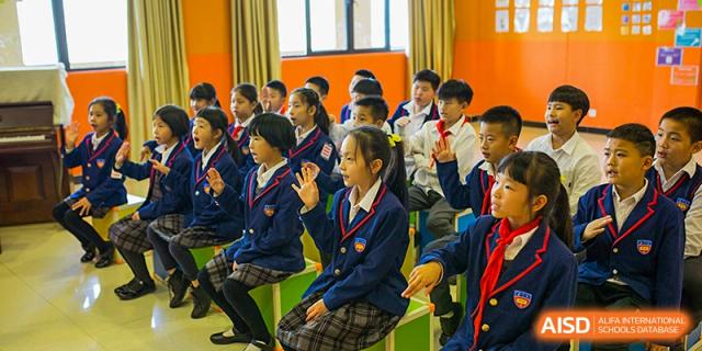 A group of female students in school uniform seated in a classroom, smiling and giving a peace sign to the camera at Wuhan Aoxin Elite School.