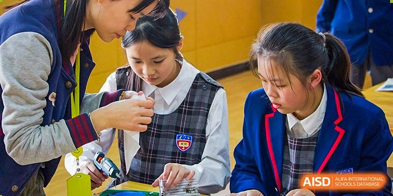 A female student in a plaid vest uniform concentrating on a task or project in a classroom at Wuhan Aoxin Elite School.