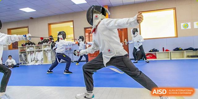 A student in full protective gear practicing fencing with a foil in an active pose during a class at Wuhan Aoxin Elite School.