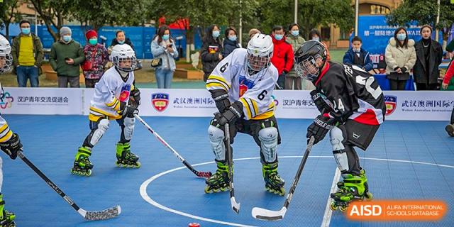 A student in full protective gear, helmet, and roller skates playing roller hockey on a blue court at Wuhan Aoxin Elite School.