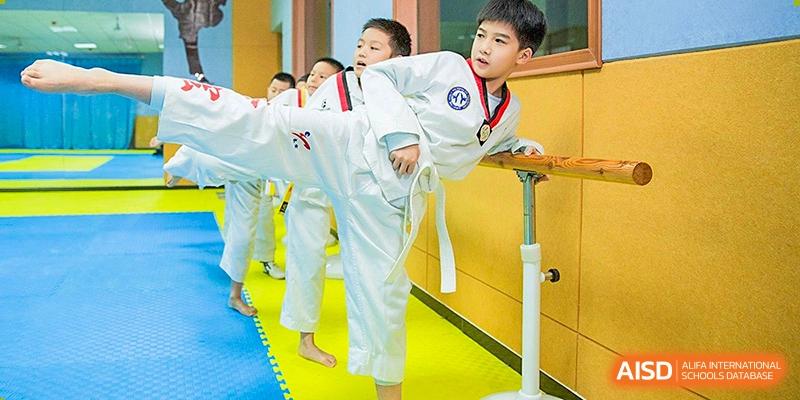 A young male student in a white Taekwondo uniform performing a high kick over a piece of equipment during martial arts practice at Wuhan Aoxin Elite School.