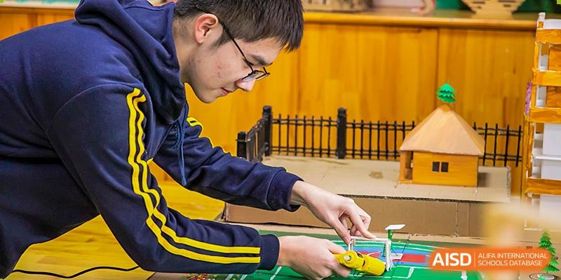 A male student in a school uniform concentrating on connecting wires or working with an electrical component during a STEM or robotics class at Wuhan Aoxin Elite School.