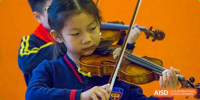 A close-up of a young student concentrating while playing the violin during a music lesson at Wuhan Aoxin Elite School.