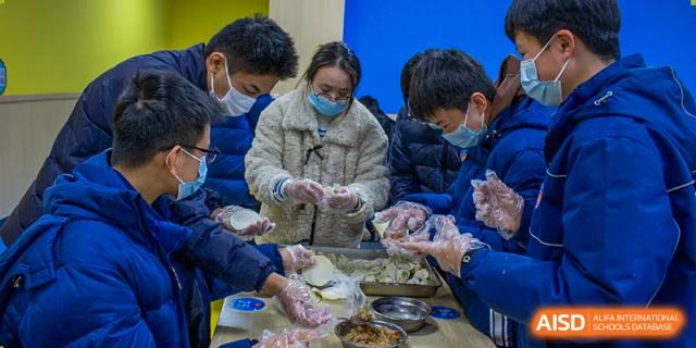 Students wearing face masks and gloves collaborating on a hands-on activity, possibly making dumplings or other food, as part of a life skills class at Wuhan Aoxin Elite School.