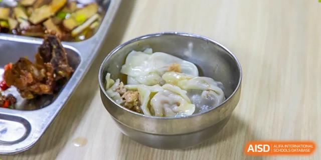 A close-up of a meal featuring a bowl of dumplings (Jiaozi or Wontons), part of the healthy school menu at Wuhan Aoxin Elite School.