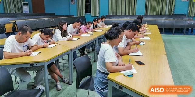 Students and teachers from the Wuhan Hongshan High School International Department participating in a lesson, seated at long tables.