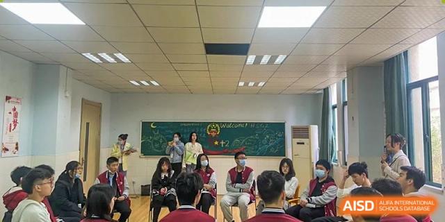 Students and teachers from Wuhan Hongshan High School International Department posing at the front of a classroom with a chalkboard.
