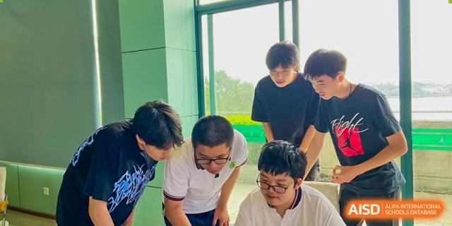 A small group of male students from Wuhan Hongshan High School International Department collaborating intently on a project by a large window.