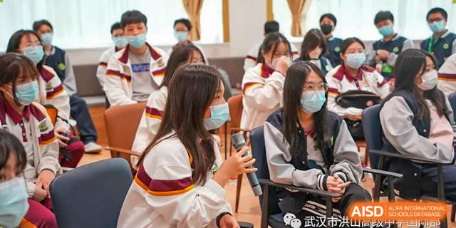 Students from Wuhan Hongshan High School International Department wearing masks and seated in graduation gowns or formal attire during an event.