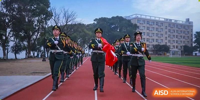 Wuhan Hongshan High School International Department students marching in uniform with a flag on a track.