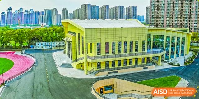 Wuhan Hongshan High School International Department - Close-up view of the modern, bright yellow building with an entrance to an underground level. Tall apartment buildings are visible in the background.