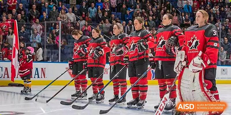 Female hockey team portrait. Wuhan Hongshan High School International Department. Four players in red & black uniforms on ice, sticks in hand, facing audience. Team spirit.