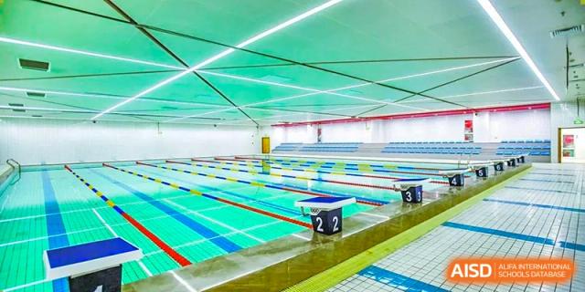 An indoor swimming pool with lanes. Wuhan Hongshan High School International Department. Bright, modern facility with blue and green tiles, a starting block marked with '2'.