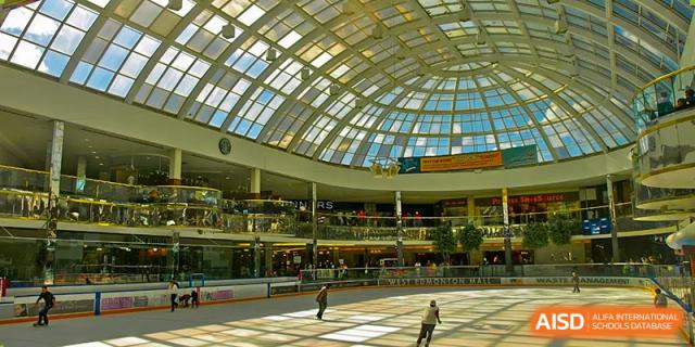 Interior of a large mall with a domed glass ceiling. Wuhan Hongshan High School International Department. People are ice skating below. A bright, modern indoor public space.