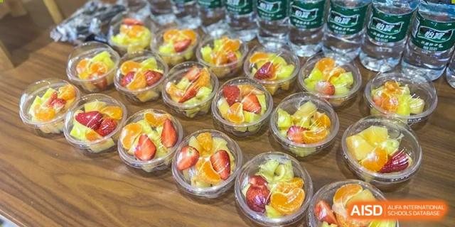 Multiple clear cups of fresh fruit salad, including oranges and strawberries, prepared for students at Wuhan Hongshan High School International Department.