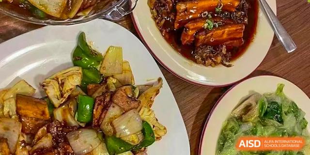 A plate of sautéed vegetables and another dish with braised meat, part of a meal or event at Wuhan Hongshan High School International Department.