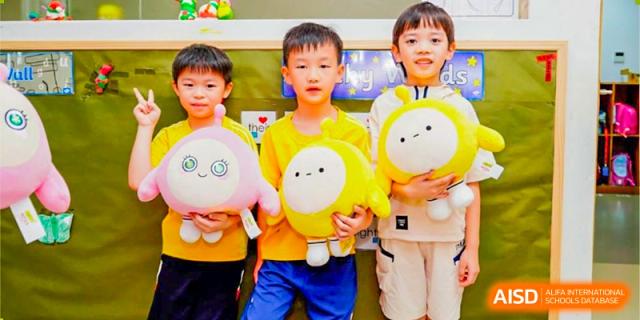 Young students from BASIS International School Guangzhou holding yellow and pink round, smiling plush toys.