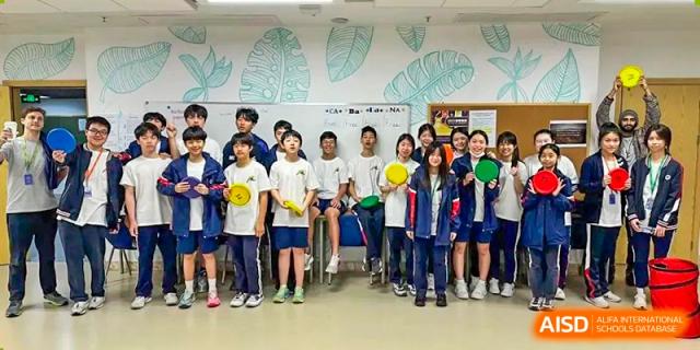 A large group of students from BASIS International School Guangzhou wearing white and yellow shirts, posing together indoors.