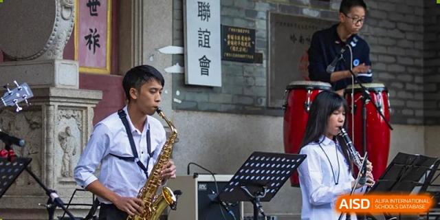 A male student from BASIS International School Guangzhou playing the saxophone during a performance next to a music stand.