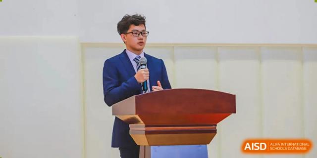 A male student from BASIS International School Guangzhou wearing a suit and glasses, speaking at a podium.