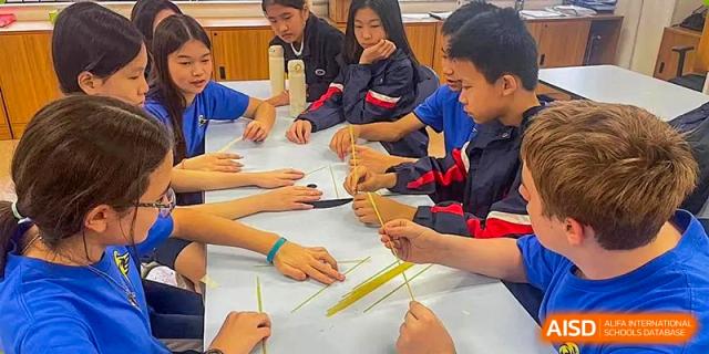Students from BASIS International School Guangzhou collaborating on a hands-on project using small wooden sticks at a table.