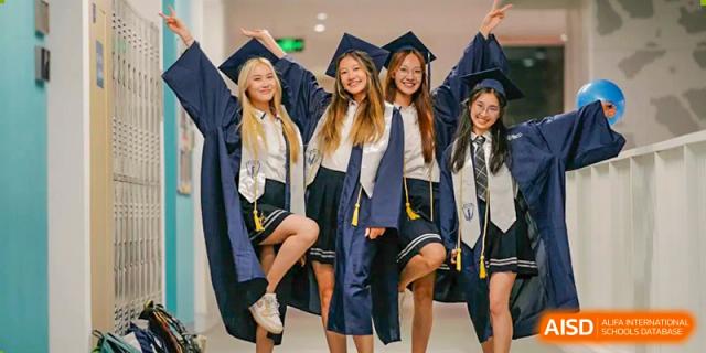 A group of graduating students from BASIS International School Guangzhou wearing caps and gowns and smiling together.