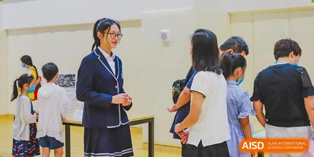 Two female students from BASIS International School Guangzhou in uniforms interacting in a brightly lit hallway.