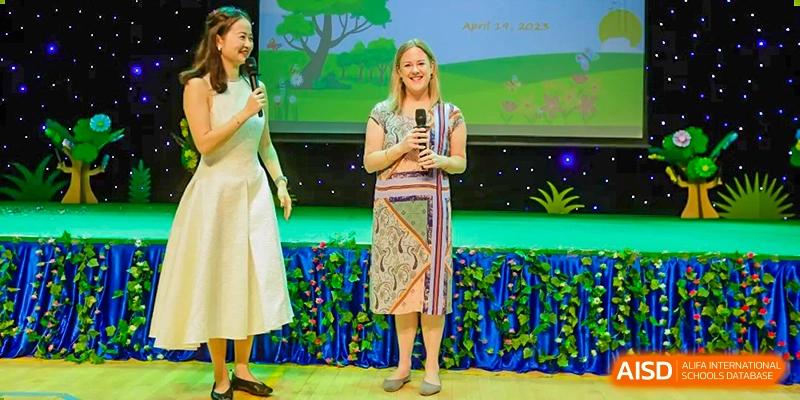 A teacher or speaker at BASIS International School Guangzhou stands on a stage with a microphone addressing an audience.