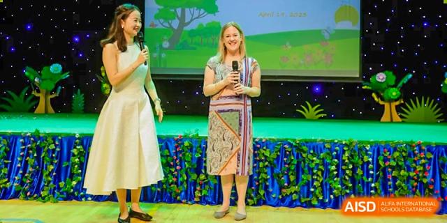 A teacher or speaker at BASIS International School Guangzhou stands on a stage with a microphone addressing an audience.