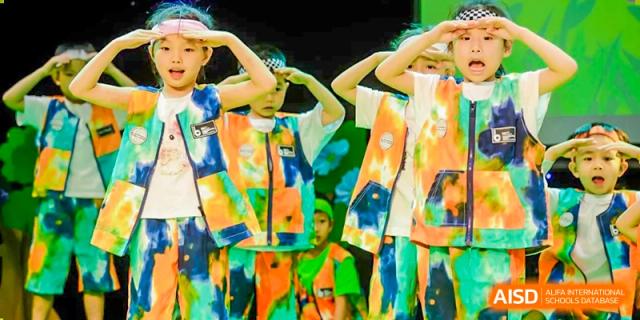A close-up of several children from BASIS International School Guangzhou in brightly colored, tie-dye-style vests performing a dance with their hands raised.