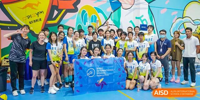 A large group of middle or high school students from BASIS International School Guangzhou posing with a blue banner displaying the school logo.