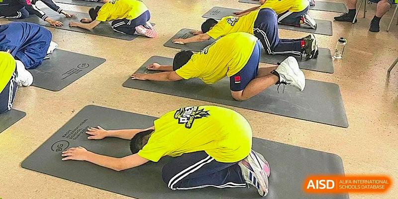 Two students from BASIS International School Guangzhou doing a floor exercise or stretch in a yellow shirt.
