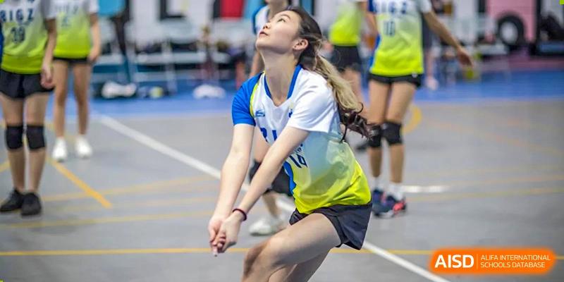 A female student from BASIS International School Guangzhou in a white and blue uniform in a defensive position, ready to bump a volleyball.