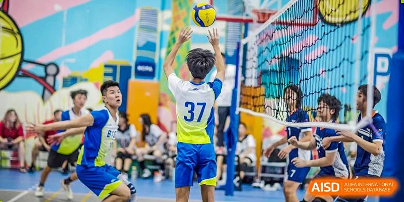 A male student from BASIS International School Guangzhou wearing a blue and yellow uniform, jumping to spike a volleyball during a game.