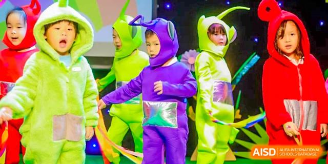 A young child from BASIS International School Guangzhou dressed in a brightly colored, purple and neon-green costume with a hood, possibly performing.