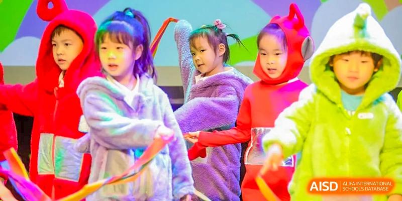 A close-up of young female students from BASIS International School Guangzhou wearing brightly colored hoodies, performing on a stage.