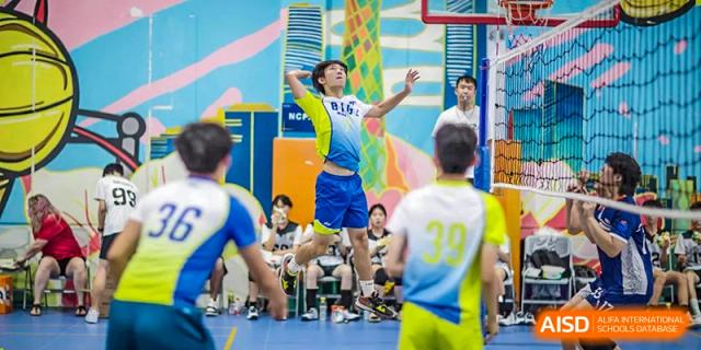 A student from BASIS International School Guangzhou wearing a blue and yellow uniform jumping up to hit a volleyball.