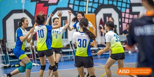 BASIS International School Guangzhou female volleyball players wearing blue and yellow uniforms celebrating a point on the court.
