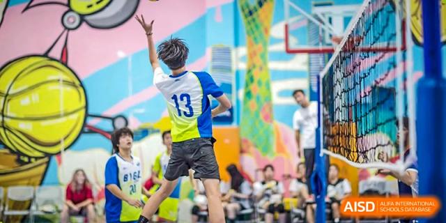 A male student from BASIS International School Guangzhou with the number 13 on his back, looking up to play volleyball on an indoor court.