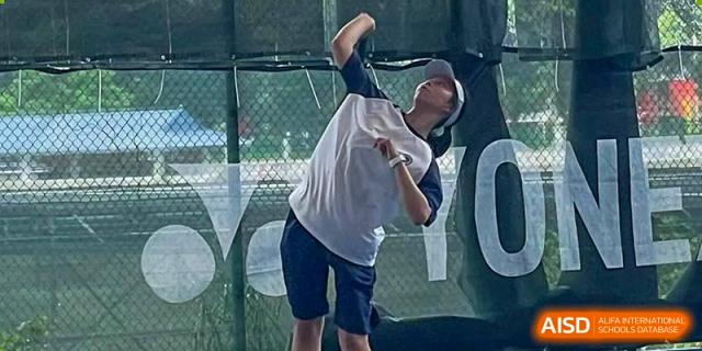 A male student from BASIS International School Guangzhou hitting a tennis serve with his back to the camera.
