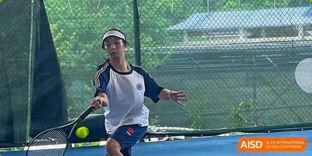 A male tennis player from BASIS International School Guangzhou in a white visor and blue and white uniform on an outdoor court.