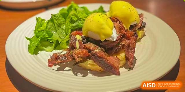 A breakfast or brunch dish featuring poached egg, bacon, and greens at BASIS International School Guangzhou.